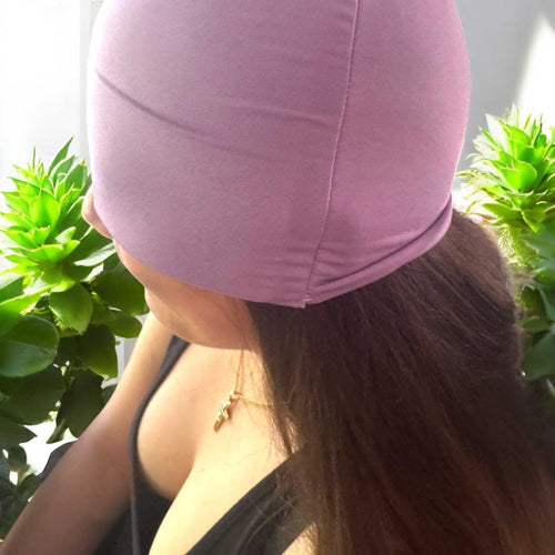Woman wearing a mauve soothing cooling cap for migraine and headache relief surrounded by green plants