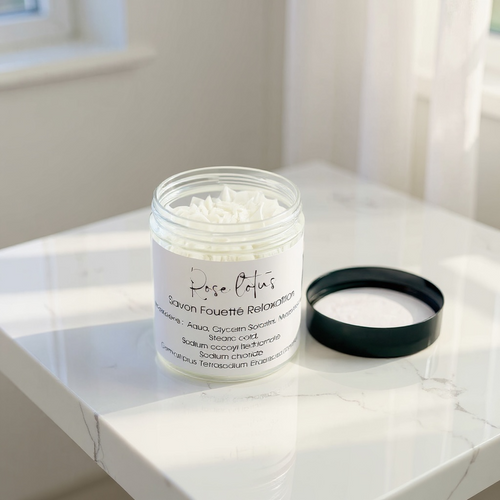 savon fouetté naturel blanc dans pot transparent avec couvercle noir sur surface en marbre blanc sous lumière naturelle