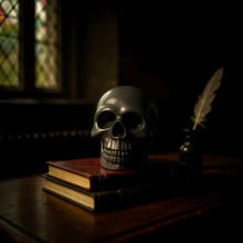 Charger l&#39;image dans la galerie, Black skull-shaped glycerin soap on vintage books in dimly lit room
