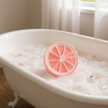 Charger l&#39;image dans la galerie, Bombe de bain effervescente en forme de tranche de fruit flottant dans une baignoire remplie de mousse, ambiance naturelle et relaxante.
