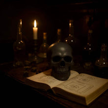 Charger l&#39;image dans la galerie, Black skull-shaped vegetal glycerin soap on an open book with candlelight ambiance
