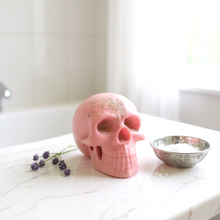 Charger l&#39;image dans la galerie, Pink glycerine soap shaped like a skull on a bathroom counter with lavender sprigs and a silver bowl of bath salt nearby
